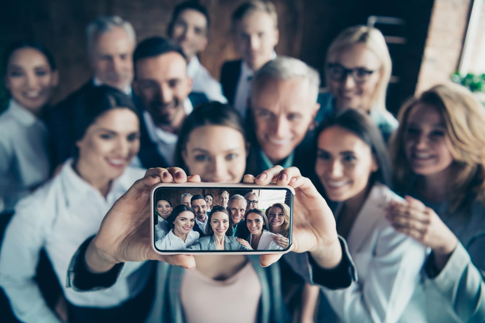 Close up blurry photo business people different age race free time excited team building hug embrace cuddle she her he him his telephone smart phone make take selfies formal wear jackets shirts.
